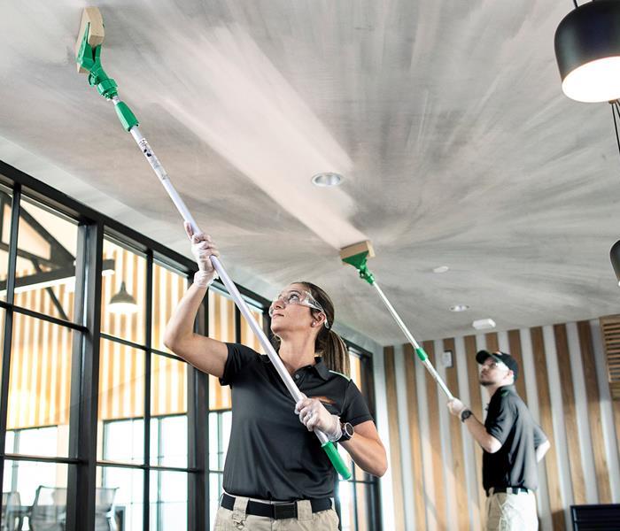 Two SERVPRO technicians cleaning soot from an office ceiling.
