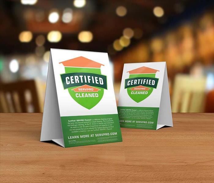 Table tent signs describing the Certified: SERVPRO Cleaned program on top of a wooden table.